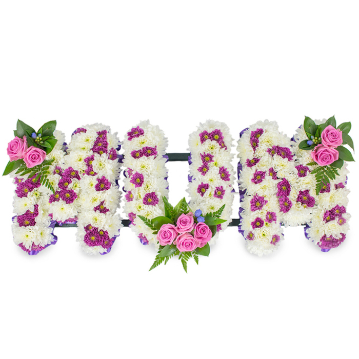 Against a plain white field stands a three-dimensional floral composition spelling MUM, each letter lovingly formed from a dense matrix of ivory-white chrysanthemum blooms that create a velvety, cloud-like texture. The arrangement keeps a classic palette but introduces depth through carefully placed pops of colour: small magenta and purple spray chrysanthemums are interspersed among the white to create subtle shadow and pattern across each letter face. Pink spray roses serve as warm focal bouquets - a delicate cluster at the upper left of the first M, a fuller cluster cradled in the lower curve of the U, and a matching group at the upper right of the second M - each wrapped visually by lush dark green foliage and soft fern fronds that sweep around the roses and spill slightly onto the white chrysanthemum field. Tiny cobalt-blue accent flowers are used sparingly for bright punctuation, their cool tones balancing the pinks and purples. Along the edges of the letters a faint purple ribbon suggests a refined outline while a slender dark bar connects the three letters at their base, giving the tribute cohesion and a quiet formality appropriate for a funeral setting. The overall scent is a gentle wash of fresh chrysanthemum with the faint, sweet lift of roses; the feeling evoked is comforting and respectful. Crafted with local care in the Golders Green area, this personalised memorial piece combines traditional sympathy whites with thoughtful colour to honour a mother's memory with dignity and tenderness.