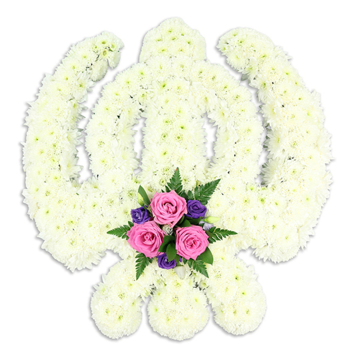 A carefully composed floral Khanda, the revered emblem of Sikhism, is presented against a clean white backdrop, allowing every curve and line of the tribute to stand out with clarity and grace. The entire symbol - from the central upright double-edged sword to the smooth circular chakkar that surrounds it, and the two crossed kirpans sweeping outward at the base - is densely formed from small white chrysanthemum florets or similar compact blossoms. These flowers are packed so closely that they create a continuous, velvety surface, their softly ruffled petals lending a gentle, almost quilted texture. Subtle variations of white and pale cream catch the light, giving the tribute depth and quiet luminosity, much like the calm early-morning brightness over Golders Green Road. At the lower centre of the design, in the cradle formed where the kirpans meet, a small yet vivid cluster of accent flowers creates a poignant focal point. Three rich pink roses, at that perfect stage of openness where the spiral of petals is clearly defined but not yet fully unfurled, sit at the heart of this cluster. They are framed by smaller, deep purple blooms, perhaps lisianthus or freesia, whose darker tones bring a dignified contrast. Wisps of dark green fern and glossy foliage weave through the accent posy, adding freshness and natural movement. A faint, soft-edged shadow beneath the Khanda suggests dimension and solidity, as if the tribute rests on a stand at the front of a Gurdwara or chapel near Golders Green Crematorium. Designed for Sikh funerals, memorial services, and commemorations, this floral Khanda offers a serene and heartfelt expression of faith, honour, and eternal remembrance, crafted with the care of an experienced local florist serving families across Golders Green and the surrounding North West London community.