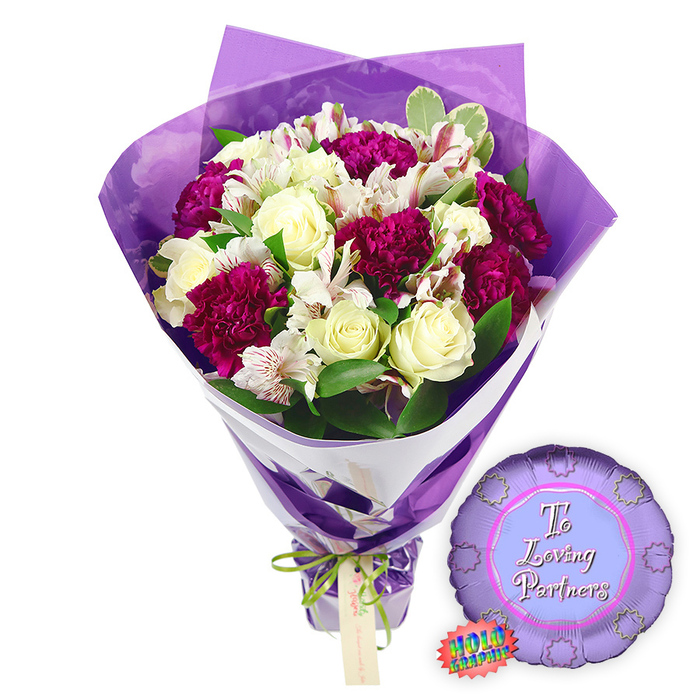 A thoughtfully styled romantic gift set is displayed against a pure white background, showcasing both the intricacy of the flowers and the playful charm of a celebratory balloon. At the core is a hand-tied bouquet shaped into a generous dome, brimming with creamy white roses whose spiralled petals remain gently closed, promising long-lasting freshness for couples around Golders Green. Interlaced with the roses are numerous deep magenta to burgundy carnations, their tightly packed, ruffled petals creating a sense of plush volume and rich colour, like velvet cushions nestled between the softer blooms. Delicate white alstroemeria flowers weave through the arrangement, each petal decorated with fine reddish-brown speckles and stripes on the inner surface, adding a refined, almost painterly detail. Around these focal blooms, glossy green leaves and touches of variegated foliage fan outward, echoing the leafy calm of Temple Fortune and the nearby parks. The entire bouquet is wrapped with an eye for modern style: a base layer of crisp white paper gives structural support and a clean edge along the stems, while an outer layer of translucent, crinkled purple film rises above the flowers, forming soft peaks that frame the bouquet and catch the light in gentle reflections. At the gathered base, a slender bright green satin ribbon is tied into a tidy bow, a small light brown gift tag hanging discreetly from the knot, ready for a handwritten message from a loving partner. To the right side of the bouquet lies a metallic purple round foil balloon with a distinctive scalloped, rosette-like border, evoking the look of an award ribbon. Inside its lighter purple centre, the phrase To Loving Partners appears in elegant pink script, with a small rainbow holographic sticker affixed near the lower edge, suggesting a special shimmering finish. Together, this bouquet and balloon capture the warmth of shared milestones and quiet evenings at home, making them ideal for anniversaries, proposals, or romantic surprises delivered across NW11.