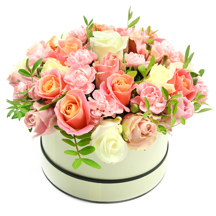 A sophisticated, handcrafted hatbox arrangement presented in a round cream container, detailed with two thin dark bands around its rim and base, creates a lush, domed bouquet against a pure white background. The composition features abundant roses in varying stages of bloom, their centres rich with coral-peach and soft apricot tones that gently transition to blush pink and creamy ivory on outer petals. Interlaced among these larger roses are numerous light pink carnations, their frilly, ruffled textures filling negative space and adding a soft, cloud-like depth to the presentation. Small, elongated green leaves emerge intermittently, providing slender lines of freshness that contrast with the rounded floral forms and enhance the bouquet's three-dimensionality. Under soft, flattering light the petals exhibit a velvety sheen and subtle gradations of colour, while the implied scent is a tender, powdery sweetness - a fragrance that evokes quiet mornings spent in Golders Hill Park or browsing the independent shops near Golders Green Road. This arrangement, lovingly assembled by Flowers Golders Green, speaks of considered craftsmanship and is suited to romance, celebrations, gratitude, and comforting gestures alike - birthdays, anniversaries, Mother's Day or a refined sympathy tribute. Designed to be both intimate and luxurious, it can be delivered locally across Golders Green and neighbouring Hampstead, presented as a premium floral gift that marries classic elegance with contemporary sensibility. Every bloom is placed with an eye for balance, creating an inviting, tactile invitation to pause and enjoy the moment.