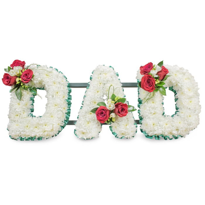 A dignified and tender floral tribute spells out DAD in large, three-dimensional capital letters, each letter densely layered with hundreds of pristine white chrysanthemums to create a seamless, soft-textured surface that reads of purity and steadfast love. A deep emerald green pleated ribbon traces each letter's edge, providing crisp contrast and architectural clarity against the white blooms. Each of the three letters is decorated with a carefully composed cluster of deep red roses, fragrant white freesia and lush green foliage: the left D bears an abundant spray on its upper curve, the A holds a similar arrangement near its left stem with a delicate loop of foliage reaching up, and the right D mirrors the first with another elegant bouquet. Thin, dark green structural bars are visible behind the letters, discreetly connecting and supporting the display so it sits with poise at a service or graveside. Set against a bright, even white background and photographed in soft natural light, the fine textures of chrysanthemum petals, the velvety depth of rose petals and the crisp sheen of foliage are all clearly articulated. This bespoke design, created by Flowers Golders Green with sensitivity to local customs and the quiet settings of nearby Golders Hill Park and the Golders Green Crematorium, offers a personalised and lasting way to honour a father. The combination of white chrysanthemums for devoted remembrance and red roses for deep affection makes this arrangement both visually striking and emotionally resonant for mourners and readers alike.