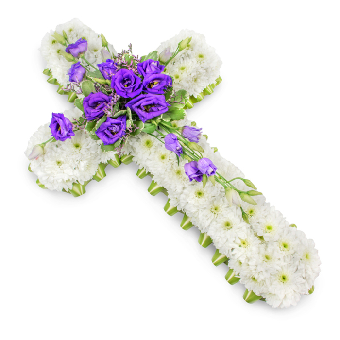 The image shows a beautifully detailed floral cross, designed as a funeral tribute, positioned against a seamless white background so that every petal can be clearly seen. The cross itself is entirely covered in compact white spray chrysanthemums, their small, closely set petals forming a plush, almost quilted surface. Each flower appears fresh and carefully placed, contributing to an overall impression of purity and tranquillity. The tiny light-green centres of the chrysanthemums provide just enough colour variation to give the design depth without detracting from its calm, monochrome character. Around the perimeter of the cross, a slim band of bright lime-green ribbon or binding frames the flowers, following the straight arms and neat corners. This edging neatly defines the shape, adding a subtle, contemporary touch while still remaining respectful and understated. At the meeting point of the vertical and horizontal arms sits a generous cluster of deep purple lisianthus blooms. Their layered petals and velvety texture draw the eye immediately, offering a rich, dignified contrast to the white base. Among the lisianthus are tiny accents of soft foliage and a few delicate filler flowers, which soften the transitions and lend a natural, garden-inspired feel. From this central feature, a gentle spray of lisianthus blooms and buds flows diagonally down the right-hand side of the cross, suggesting a tender, cascading motion. The lighting is soft and even, casting a subtle shadow beneath the floral piece and giving it a gentle three-dimensional presence. This kind of floral cross, often requested for church services or graveside tributes around Golders Green and nearby Temple Fortune, is a thoughtful way to honour a loved one with a symbol of faith, remembrance, and enduring love.