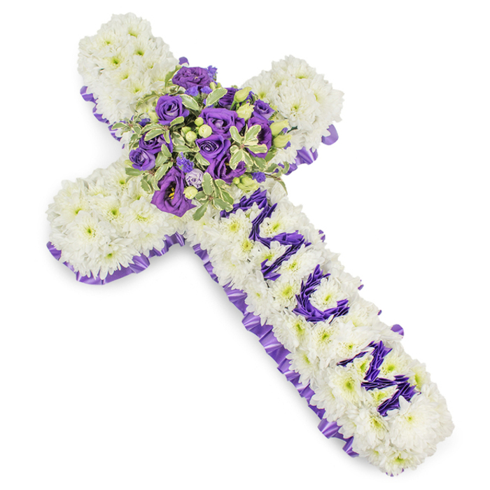 A large, reverent Christian cross made entirely from pristine white chrysanthemum blooms commands attention with its immaculate, cushiony surface, each floret placed with precision to create a uniform field of white. Encircling the entire shape is a meticulously ruffled purple satin ribbon-an elegant, solemn border whose rich hue ranges from lilac to deep violet as it catches the light. Running down the central shaft, the name MUM is spelled out in clearly shaped letters composed of smaller purple blossoms-likely lisianthus or spray chrysanthemums-whose concentrated colour provides a poignant contrast against the white background. Anchoring the composition at the intersection of the arms is a generous central spray of purple tones: velvety deep violet roses paired with paler lavender roses and soft lisianthus, their layered petals lending both depth and a gentle movement to the heart of the cross. Variegated foliage, leaves highlighted with lighter edges and darker centres, fans around the flowers to add texture, while the occasional small green berry introduces a subtle, natural accent.

Presented on a stark white backdrop that allows the whites and purples to read with clarity, this tribute radiates dignity and serenity. The cool colour story evokes peace and remembrance, the dense petal work offers a comforting solidity, and the overall craftsmanship is suited for memorial services at places such as Golders Green Crematorium or local chapels along Finchley Road. The arrangement feels like a calm, floral benediction-measured, personal, and profoundly respectful.