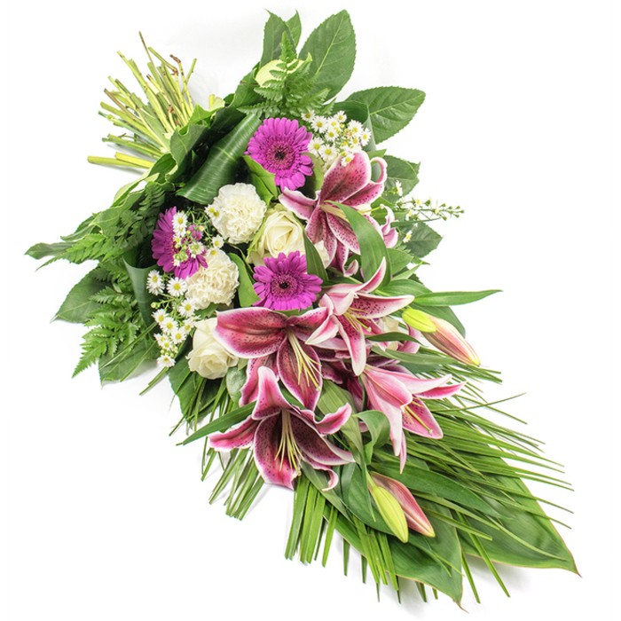 A beautifully composed funeral sheaf is displayed on a bright white backdrop, its colours and contours clear and unhurried, like a thoughtful farewell shared in one of Golders Green's peaceful side streets. The design flows diagonally from the bound stems at the top left down to a soft point at the bottom right, forming an elongated teardrop that suggests both movement and rest. Dominating the centre are several Stargazer lilies in full and partial bloom, their wide petals a deep magenta-pink washed with white along the edges and speckled with burgundy, creating a dramatic yet gentle focal point. Interspersed with these are closed and half-open buds, pale green flushed with pink, promising a continuation of beauty over the coming days. Nestled between the lilies, bright magenta gerbera daisies provide vivid, disk-shaped bursts of colour, while creamy white roses and frilled white carnations add a quiet, dignified softness. Fine clusters of tiny white daisy-like flowers are scattered through the arrangement, giving a delicate, airy texture that lightens the overall design. The flowers are supported by a rich frame of foliage: broad, glossy dark green leaves form a sturdy base, while feathered fern fronds and lighter, grass-like leaves extend outward and downward, accentuating the spray's length and gentle cascade. The lighting is even and natural, revealing the subtle sheen of petals and the velvety depth of the greenery. Crafted in the tradition favoured by many families in Golders Green and nearby Hampstead and Cricklewood, this arrangement is a touching tribute for funerals, memorial services, or sending condolences, conveying respect, love, and remembrance without a single spoken word.