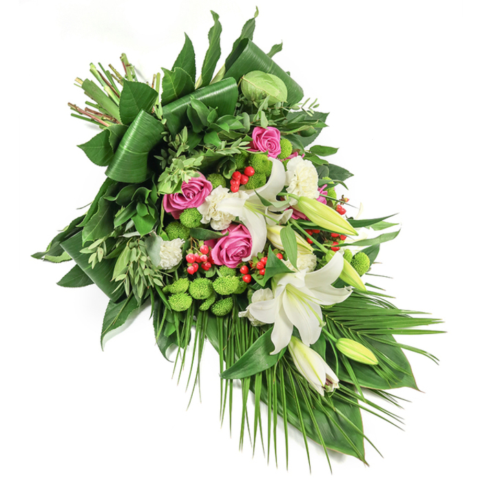 Arranged with the skill and empathy of a Golders Green florist, this striking sympathy spray features a rich tapestry of blossoms cascading from the upper left to lower right, set against a stark white background. Prominent throughout are elegant white lilies, their stately, open blooms revealing golden stamens, accompanied by closed buds that hint at the promise of new beginnings. Interwoven are clusters of deep pink and vibrant fuchsia roses, each petal delicately unfurling and reminiscent of the blossoming gardens near Hoop Lane or the restful spaces of Hampstead Heath Extension. Vivid green santini chrysanthemums appear in rounded, moss-like clusters, imparting both energetic texture and a refreshing burst of colour. Smaller, ruffled white carnations fill in spaces, softening transitions between large blooms and enhancing the arrangement's lushness. Brilliant red hypericum berries are thoughtfully placed, providing a lively visual accent amidst the lush green backdrop. That backdrop features an array of foliage: glossy, broad-leaved greens-some artistically shaped to provide strong lines-mingled with lighter, finer sprigs and elegant palm fronds that trail gracefully downward, reinforcing the bouquet's flowing design. The blend of flower types, colours, and textures creates an atmosphere of serenity and remembrance, ideally suited for heartfelt condolences, thoughtful funeral tributes, or memorial gestures across Golders Green. Soft daylight, evocative of peaceful mornings on Finchley Road, accentuates every detail, bringing out a sense of unity and hope for those grieving or remembering a loved one.