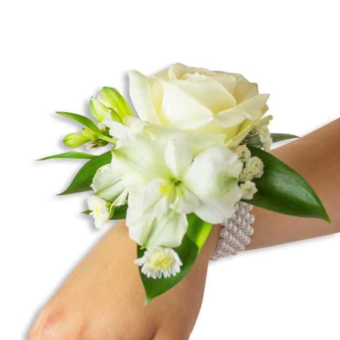 Displayed against a pure white backdrop, this wrist corsage rests on a fair-skinned wrist angled slightly upward from the lower right into the centre, offering a close study in soft whites and rich greens. The focal point is a creamy ivory rose, petals unfurling in tender concentric curves that reflect a soft studio light and convey a quiet luxury. Beneath and to the left, a larger trumpet-style white bloom - reminiscent of alstroemeria or a small lily - presents a pale lime-green throat and gently ribbed petals that add structure and visual depth. Tiny green-tinged buds pepper the arrangement, suggesting movement and future opening, while feathery sprays of baby's breath (gypsophila) weave a translucent veil around the main blossoms. A grouping of small, daisy-like white florets with vivid yellow centres anchors the lower edge of the cluster with a cheerful, contrasting dot of colour.

Several broad, glossy dark-green leaves with a slightly waxy texture frame and support the flowers, their surfaces catching light and enhancing the white blooms' purity. The corsage is secured to the wrist by a refined multi-strand bracelet of round, luminous white pearls that encircle the arm with gentle elasticity, providing both stability and an elegant companion to the flowers. This combination of textures - satiny rose petals, crisp green leaves, airy filler, and smooth pearls - creates a tactile harmony ideal for formal occasions: weddings, proms, or evening receptions in Golders Green, near Golders Hill Park or Temple Fortune. The scent is fresh, faintly floral, and the overall impression is one of handcrafted restraint and heartfelt celebration.