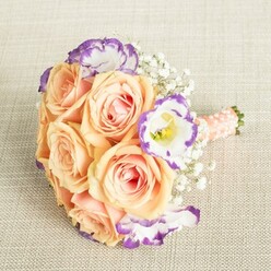 In the heart of Golders Green, this bouquet tells a story as gentle as a morning stroll past Hampstead Heath Extension. Plump roses in dreamy shades of peach and apricot nestle together, kissed by soft sunlight and unfolding with hints of delicate blush pink in their centres, suggestive of early summer's promise. Ruffled lisianthus, their petals haloed in lively purple, add a painterly contrast against the creamy blooms, their unique shapes drawing the eye. Wisps of baby's breath, airy and cloudlike, weave through the bouquet, creating a sense of weightless romance - much like the easy warmth of community gatherings near Golders Green station. The stems are meticulously bound with silken ribbon, the gentle peach-pink hue complemented by carefully arranged pearl beads, an homage to subtle elegance. This arrangement reflects both artistry and tradition, embodying the care and local knowledge of Flowers Golders Green. It's a bouquet for moments that matter, whether destined for the hands of a bridesmaid in an NW11 celebration or displayed as a symbol of affection at a gathering on Golders Green Road. Every bloom, bead, and ribbon is thoughtfully placed, capturing the refined beauty and heartfelt meaning that define local floral craftsmanship.