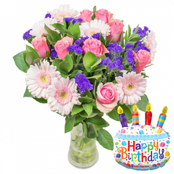 Captured in soft, natural light against a clean white backdrop, this joyful birthday arrangement blends romantic pinks with lively purples and glossy foliage. At the heart of the design are numerous soft-pink roses, their petals layered and slightly cupped, graduating from pale blush at the edges to a richer rose-pink toward the centers, evoking warmth and affectionate sentiment. Pale pink Gerbera daisies sit among the roses, their broad petals forming cheerful discs with pale, buttery centres that lift the composition with a touch of classic charm. The bouquet's texture is enlivened by abundant clumps of deep purple statice or limonium, which provide crisp, papery contrast and a three-dimensional ripple throughout the mass of blooms. Healthy, deep green leaves frame and support the flowers, their glossy surfaces catching the light and reinforcing the fresh, just-arrived-from-the-market feel. Arranged in a simple, clear glass vase filled with water, the visible stems suggest careful preparation by an experienced florist. To the right, a cake-shaped foil balloon decorated with white 'icing,' a blue scalloped border, colorful sprinkles and four multi-coloured candles proclaims "Happy Birthday" in playful, bright letters, while a small "KALEIDOSCOPE" logo sits at the bottom edge. The image reads as a complete birthday gift-visually balanced, fragrant in imagination, and perfect for delivery to a Golders Green home or for pickup on Golders Green Road or near Golders Hill Park when you want to combine classic floristry with a fun celebratory accent.