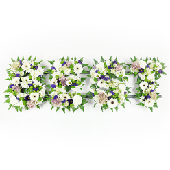 An intimate, three-dimensional letter tribute spelling DAD, rendered in a serene palette of whites, purples, and lush greens and arranged with the practiced hand of a local florist. Each letter is a compact tapestry: velvet-like chrysanthemum heads and ivory gerberas provide broad, luminous surfaces while pale coffee-tinged roses and creamy lisianthus introduce a softer, more romantic curve. Deeper violet statice and small mauve roses appear as thoughtful punctuation, whispering warmth into the predominantly white composition. Sprightly green button chrysanthemums dot the arrangement, adding freshness and a lively, tactile contrast, while abundant fern fronds outline each letter with feathery motion that both frames and softens the shapes. The blooms rest on a dark grey or near-black foam base that gives structural clarity to every stroke of the lettering, visible only where petals part to reveal it. The scent is subtle: a clean floral note with the green sharpness of freshly cut stems. As a sympathy piece, the arrangement reads as both a declaration of love and a calm, composed farewell - something families in Golders Green might choose for a service at a local chapel or to lay beside a photograph at a wake. Prepared with local knowledge and care by Flowers Golders Green, this tribute balances botanical texture, heartfelt sentiment, and quiet dignity to honour the memory of a father in a way that feels both personal and beautifully measured.