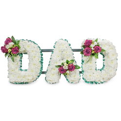 This photograph presents a respectfully crafted funeral lettering piece that reads "DAD" in large, sculpted capitals, each formed from a thick mass of pure white chrysanthemums that create a soft, pillowy surface. The letters are crisply defined by a vivid emerald green ribbon with a pleated, ruffled finish that traces both the outer and inner contours, producing a refined contrast between the cool green border and the warm white blooms. A subtle dark green or slate-grey support bar passes behind the letters, hinting at a sturdy, stand-ready design for display at a service or a graveside. Carefully placed floral accents lift the overall composition: the first 'D' bears a cluster on its upper left curve, the 'A' cradles a bouquet in the lower V, and the final 'D' is accented on the upper right curve - each cluster composed of rich magenta roses, small white freesia or spray blossoms, and deep, glossy foliage for depth. The sensory impression is understated - the soft, powdery texture of the chrysanthemums, the discreet perfume of roses, and the green, almost citrusy lift of freesia. A florist familiar with Golders Green and surrounding streets like Finchley Road might arrange this for a service at Golders Green Crematorium or a quiet memorial by local parks; its balance of tradition and personal warmth makes it a dignified expression of love and farewell.