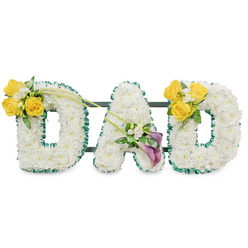 Arranged with careful craftsmanship in the north London tradition, this freestanding floral tribute spells DAD in three large, rounded block letters formed from a dense blanket of pristine white spray chrysanthemums. Each letter's edge is traced with a ruffled, rich dark-green satin ribbon that gives a crisp silhouette and a formal, respectful outline against the white. Behind the letters, slim dark green metal bars are discreetly visible, connecting and supporting the trio so they read as one cohesive memorial display against the plain white backdrop. The lighting is soft and even, highlighting the texture of the small florets and the satin sheen of the ribbon without dramatic shadow.  Floral accents are placed with thoughtful balance. The left D carries a radiant cluster of bright yellow roses on its upper left curve-about three to four blooms-nestled with small white fillers such as freesias and light green foliage; from this group two long, slender green stems reach diagonally toward the centre, adding a graceful line. The central A features a low-side arrangement of two deep purple or burgundy calla lilies whose sculptural trumpets create a quiet, noble focal point, surrounded by tiny white sprays. The right D mirrors the left with a matching sunny rose cluster. From our Flowers Golders Green studio near Golders Green tube and the crematorium, we often assemble pieces like this for services on Hoop Lane or quiet commemorations at Golders Hill Park-an arrangement that balances purity, warmth, and reverence for a father's farewell.