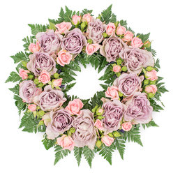 A serene, circular funeral wreath is photographed from above on a clean white background, its symmetry immediately drawing the eye to the unbroken ring of flowers. The design is luxurious yet restrained, built almost entirely from roses in soft, contemplative shades that would feel at home in any quiet chapel or house in Golders Green. Large, fully open roses in dusty lavender and muted mauve form the backbone of the arrangement, each bloom lush with layered petals that curl and fold like silk. Their greyish-purple tones create a gentle, vintage mood-neither bright nor sombre, but softly reflective. Nestled between them are sprays of petite blush-pink roses, some still in bud, others just beginning to open, adding a delicate contrast and a sense of time gently passing. These smaller blooms introduce a lighter, more youthful note, while keeping within the same hushed pastel palette. The flowers sit on a dense collar of deep green fern fronds, their fine, serrated leaflets radiating outward to create a natural, feathery frame. Tiny touches of darker foliage and subtle filler buds are tucked between the roses, breaking up the colour blocks and giving the wreath depth and texture, as though it were gathered from a well-kept garden near Golders Hill Park. The light is soft and even, illuminating every petal and leaf without glare, enhancing the wreath's peaceful character. This is the sort of carefully crafted tribute that might be sent for a funeral, memorial, or graveside service in Golders Green, expressing condolences, remembrance, and the circle of life with quiet dignity and enduring grace.