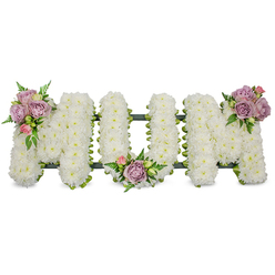 A carefully sculpted floral tribute spells the word "MUM" in large, capital letters, each letter densely covered with hundreds - perhaps thousands - of pristine white chrysanthemums or similar petite white blooms that give a soft, cloud-like texture under gentle light. The clean white surface reads as a symbol of purity and peace, its compact petals forming a uniformly luminous field that seems almost tactile. Accenting the crisp white are three small, artful clusters of pastel blooms: soft lavender roses with their powdery lilac tones, blush-pink rosebuds both closed and half-open, and fresh green leaves with delicate fern-like fronds that add movement and a cool, botanical scent. One cluster rests on the upper left arm of the first 'M', another nestles in the low curve of the 'U', and a third highlights the upper right arm of the final 'M', creating a considered, triangular balance. A dark green structural frame - possibly ribbon-wrapped or moss-covered - is visible beneath the flowers as a subtle outline and base, ensuring the letters stand with dignity and shape. The arrangement conveys quiet remembrance and deep affection, a traditional sympathy piece suitable for service, chapel, or graveside. As a local Golders Green florist would observe, the restrained palette and classic form are commonly chosen by families from surrounding streets such as Golders Green Road and Finchley Road, where soft pastels and clean whites are preferred for commemorating a mother with gentle, understated grace.