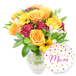 This bright, heartfelt gift set is photographed on a pristine white backdrop and presented in a clear glass vase that reveals the neat, water-filled stems beneath. Dominating the left side, a cluster of large, peach-to-orange roses unfolds in soft, velvety spirals, their warm tones giving the bouquet an immediate glow. Interspersed slices of sunshine come from yellow gerbera daisies, their flat, cheerful heads and dark central discs catching the eye and lifting the mood. Ruffled burgundy carnations bring depth and tactile contrast, their dense petals pushing gently through the bouquet to create pockets of shadow and richness. Fine sprays of white alstroemeria, with slender petals and subtle speckling, offer delicate punctuation and a whisper of fragrance, while a mix of glossy broad leaves and slim green sprigs weaves natural structure through the blooms. Nestled to the bottom-right and overlapping the vase, a glossy white Mylar balloon playfully punctuates the gift: printed with scattered gold and fuchsia polka dots and tiny hearts, it bears the flowing hot-pink words "best Mum" in a friendly script. The whole presentation-flowers, foliage, visible stems, and the personalised balloon-reads as a thoughtful, locally made gesture suitable for Mother's Day or a special birthday. Prepared with the care you expect in Golders Green, this bouquet is ideal for hand delivery across Golders Green Road, near Golders Hill Park and the tube station, and can be arranged for same-day delivery when available from Flowers Golders Green.