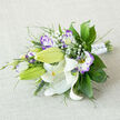 Resting on a neutral, light beige linen, this horizontally arranged bouquet reads like a crafted moment captured by an experienced local florist: large, pristine white Oriental lilies form the central focus, their satin-smooth petals arching back to expose golden-orange stamens speckled with dark pollen and delicate reddish-brown markings that add quiet character. Several lilies hold as tight green buds, a visual promise of unfolding life. Interspersed among them, white and purple lisianthus (eustoma) offer ruffled textures-petals soft and layered, fading from a creamy centre to a lively lilac or deep violet fringe that frames each bloom. Small, cloud-like bunches of Baby's Breath thread through the arrangement, introducing lightness and playful negative space between the dominant flowers.

The supporting foliage is rich and varied: broad, deep-green leaves likely ruscus or salal provide a glossy backdrop, while feathery fronds and slender spike grasses add contrast and movement. The stems are bound in a neat white satin wrap, secured with tiny, gem-like pins that catch the light and lend an understated celebratory detail. The composition is slightly asymmetrical but balanced, conveying natural grace rather than strict formality.

As a Golders Green florist product, this bouquet-available for local delivery across Golders Green and nearby Finchley Road-carries a soft fragrance where the lilies' gentle spice meets the sweet notes of eustoma. Photographed in soft morning light, it feels ideal for a wedding bouquet, an intimate anniversary, or as a tasteful gift for family and friends in the neighbourhood, reflecting the refined, seasonal sensibility of Flowers Golders Green.