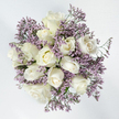 Viewed from directly above, this bouquet appears as a serene, circular pool of white and lavender, carefully crafted to express quiet sympathy. At its centre, about a dozen white roses unfold in different stages of bloom, some remaining as firm, tightly held buds, while others reveal layers of velvety petals spiralling out in soft, creamy waves. Their colour is an elegant white with a whisper of ivory at the core, which keeps the arrangement warm and inviting rather than stark. Threaded between and around these larger blooms, delicate sprays of lavender limonium stretch outward, each slender stem carrying clusters of tiny, papery purple flowers that create a light, mist-like surround. This contrast between the plush, full-bodied roses and the fine, airy filler flowers adds both visual depth and a gentle sense of movement, as though a soft breeze might be passing through. The bouquet is photographed against a bright white background, enhancing the feeling of purity and stillness, much like the calm you might feel walking through a quiet corner of Golders Hill Park on a reflective day. A few glimpses of green stems and modest foliage appear beneath the blossoms, just enough to anchor the design without disturbing its minimal, harmonious palette. The overall impression is of a thoughtfully considered tribute, suited to condolence visits and remembrance services across Golders Green and the surrounding neighbourhoods. It is an arrangement that seems to speak in a low, reassuring voice, offering comfort, respect, and a graceful farewell when emotions run deep.