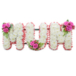 A serene, standing floral tribute spelling the letters MUM, each letter lovingly built from a dense carpet of pure white chrysanthemums that give the display a soft, cloud-like texture. The small, tightly packed mum blooms ripple across the faces of the letters, their satin petals catching a cool, diffuse light that suggests a quiet morning service. Around the outer edges a ruffled pale-pink ribbon traces each letter, its gentle frill introducing a warm blush that softens the white and adds a motherly tenderness to the composition. Between the letters a subtle dark-green support frame is visible, its structural lines barely evident beneath the blooms but providing the solidity required for a standing memorial. Three bright accent posies punctuate the arrangement: on the upper left of the first M a compact spray of deep fuchsia roses in mixed stages of opening sits with glossy fern-like foliage and little coral-red hypericum berries; the U's inner curve is balanced by a matching cluster; and the upper right of the second M repeats the same grouping so the trio of accents leads the eye across the tribute. The scent is mild and comforting-green stems and the faint honey of chrysanthemums mingled with the richer perfume of roses-conveying respect without heaviness. As a florist working in Golders Green I picture this design placed near the Crematorium chapel or on a chapel stand at a wake, intended to offer families a dignified, personalised farewell. The overall effect is one of refined sorrow and warm remembrance: classic white for purity, soft pink for love, and vivid roses to speak of enduring affection.