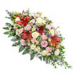 A dignified, double-ended coffin spray is shown isolated on a pure white background, emphasising its rich textures and gentle, flowing form, as if ready to be placed in a quiet chapel or crematorium in Golders Green. The arrangement is long and symmetrical, with the centre slightly fuller and both ends tapering to soft points, creating an elegant silhouette. At the core of the design, vibrant red Oriental lilies command attention, their large, star-shaped blooms opened wide, petals edged in deeper crimson and brushed with subtle speckling. These dramatic flowers are surrounded by clusters of roses in calming tones of cream, ivory, and pale pink, some blossoms open and generous, others still cupped in tighter buds, adding a sense of unfolding remembrance and enduring love. Interspersed among them, pale pink spray carnations offer a ruffled, cloud-like texture, building a sense of volume and comfort throughout the display. Delicate filler flowers in shades of lavender, lilac, and soft purple weave between the larger heads, providing gentle contrast while keeping the overall palette soothing and harmonious. Hints of blue-purple thistles or similar spiky blooms add an intriguing, slightly wild accent that prevents the spray from feeling overly formal. All of the flowers are cradled in a lush bed of dark green foliage, with broad, glossy leaves forming a strong foundation and finer, trailing greenery softening the outline at the edges. The composition feels freshly made, like a tribute carefully prepared in a local Golders Green flower shop early in the morning for same-day delivery to a funeral service, offering comfort, sympathy, and a graceful expression of farewell.