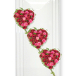 Three sumptuous heart-shaped rose tributes appear in a vertical cascade, each heart glowing with a rich blend of red and pink roses and connected by delicate trails of ivy. The hearts are positioned in a gentle diagonal from top left to bottom right, creating the impression of love flowing down through time, or perhaps three chapters in a shared story. Every heart is tightly packed with roses: velvety, deep crimson blooms suggest devoted, enduring love, while the vivid fuchsia and soft blush pink flowers soften the design with warmth, compassion, and gentle farewell. The mix of buds just beginning to open and fully unfurled flowers adds depth and dimension, as if the surface were a quilt of living petals. Fine ivy vines edge each heart, their small, fresh green leaves providing subtle contrast and gracefully linking one heart to another, symbolising connection between family members or generations. The arrangement stands against a pure white background, possibly a serene wall in a chapel or a dedicated tribute space in a Golders Green venue, with clear, even lighting that heightens the colour without casting harsh shadows. Nothing distracts from the floral artistry; instead, the eye is drawn solely to the roses and their flowing forms. This image captures a tribute that would be at home at a funeral or memorial service in and around Golders Green, expressing love, remembrance, and respect in a way that feels both intimate and elegant, like a final, beautifully crafted love letter made of flowers.