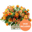 A lush and cheerful floral arrangement in vivid orange, yellow, and peach tones is set against a clean white background, its warmth echoing the friendly character of Golders Green. At the centre of the design are several rich orange roses, some with petals that softly transition into golden yellow as they approach the heart of the bloom, giving each flower a soft, glowing depth. Nestled among them are sunny yellow garden roses, tightly cupped and full of petals, adding a sense of generosity and celebration. Threaded throughout are graceful stems of peach and light orange alstroemeria, whose elongated petals and fine speckles lend an airy, painterly quality, breaking up the solid blocks of colour. Small, round, spiky orange accents-resembling safflower or thistle-are strategically placed to create playful bursts of texture, keeping the arrangement from feeling too formal. A mix of eucalyptus and other lush green foliage surrounds and supports the blooms, with silvery-green leaves and deeper tones interwoven to add depth, contrast, and a fresh, just-arrived-from-the-florist feel. The flowers are arranged in a clear, square glass vase, allowing the stems and clean water to be visible, which enhances the sense of honesty and simplicity in the design. Around the centre of the vase, a band of natural beige burlap or jute is wrapped neatly, bringing a rustic accent that would sit beautifully on a kitchen table near Golders Green Road or a windowsill close to Brent Cross. In the lower right corner of the image, a bright orange circular badge with crisp white text reads VASE INCLUDED, making it clear that this radiant, ready-to-display bouquet is delivered complete, ideal for birthdays, thank yous, or brightening a living space on a grey London day.