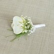 A single white orchid boutonniere rests on a softly textured, light beige fabric, its woven surface reminiscent of natural linen you might find in an elegant Golders Green bridal boutique. At the heart of the design is a pristine Phalaenopsis orchid bloom, its broad, velvety petals a pure, luminous white that gently curves around a throat touched with the faintest hint of pale yellow. This subtle warmth adds depth and a quiet sense of luxury, like morning light catching the facades along Finchley Road. Surrounding the orchid are airy clusters of white baby's breath, their countless tiny blossoms forming a delicate, cloud-like halo that softens the edges of the piece. Fine, feathery strands of fresh green foliage peek out between the blooms, their lively colour providing a graceful contrast and suggesting the feel of a peaceful walk through nearby Hampstead Garden Suburb. The stems are gathered neatly and wrapped in smooth white satin ribbon, the binding finished with a small, understated bow that signals careful, professional craftsmanship. The soft, even lighting of the image enhances every texture: the gentle sheen of the orchid's petals, the matte finish of the ribbon, and the understated weave of the background fabric. Together they create an impression of timeless elegance and calm. This boutonniere feels perfectly suited to a groom or groomsman stepping out of a car near Golders Green station on a wedding morning, ready for photographs and quiet, heartfelt vows. The overall mood is one of purity, fresh beginnings, and refined style, ideal for formal occasions where every detail is chosen with care.