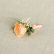 Presented from a gentle high angle, this boutonniere centres on a single apricot-peach rose whose petals unfurl in delicate spirals from a warmly coloured heart to cream-tipped edges. Each layer of petal shows a velvety texture and a subtle sheen, suggesting freshly cut bloom handled with care. Surrounding the rose are clusters of baby's breath (Gypsophila), their tiny white blossoms forming a soft, mist-like accompaniment that lifts the design and introduces an ethereal lightness. Two rolled, darker green leaves and slender, bright grass blades peek out behind the flowers, their cool tones framing the rose and creating a balanced, sculptural silhouette. The stems are bound in a coordinating peach satin ribbon tied into a small, neat bow; the ribbon's satiny finish complements the flower's softness and would feel smooth and reassuring in the fingers. A slim metallic pin is tucked at the base of the wrap, signalling the boutonniere is ready to be secured to a lapel. The arrangement rests against a finely woven ecru linen background with a subtle cross-hatch texture that echoes the ribbon and enhances the composition's timeless quality. As a local florist in Golders Green, I picture this piece on a groom at a summer wedding near Golders Hill Park or pinned for a prom night on Finchley Road; at Flowers Golders Green we craft these small accents to be modest in size but generous in sentiment, perfect for celebrations where quiet elegance matters. It reads as intimate, fresh, and quietly celebratory.