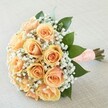 This enchanting bouquet, thoughtfully arranged in Golders Green, radiates romantic simplicity and timeless style. Soft peach and apricot roses unfurl in a tight, cohesive cluster, each petal capturing the luminous warmth of sunset across Golders Green Crescent. Encircling the roses are feathery sprays of white gypsophila, their lacy elegance reminiscent of cherished bridal veils and vintage lace from local celebrations. Polished green foliage-subtle yet vivid-frames the florals, suggesting a sense of renewal and freshness often found in the gardens and parks nearby. The stems are carefully tied with a broad, velvety ribbon in subtle peach hues, meticulously finished with dainty rows of faux pearls-this gentle embellishment bringing a touch of classic romance and tactile beauty to the arrangement. Resting atop a softly woven, neutral-toned linen background, the bouquet glows in gentle daylight. With a sweet, layered fragrance and a look that whispers promises of new beginnings, it stands as the perfect emblem for weddings and heartfelt occasions across Golders Green.