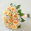 A portrait of refined tenderness, this hand-tied bouquet features creamy peach roses gathered into a perfect, rounded cluster so each bloom's velvety petals overlap like soft silk. Interspersed among them, clouds of white gypsophila add a delicate, playful texture that lifts and brightens the composition, while broad, emerald-green leaves provide a natural framework that keeps the silhouette graceful and grounded. The stems are neatly wrapped in a peach satin ribbon dotted with pearl accents, the finish intentionally tactile-inviting fingers to trace the ribbon's soft sheen and the stems' steady lines. Under diffuse daylight, the bouquet emits a gentle luminosity; the pastel apricot tones read warm but never bold, carrying an atmosphere of calm anticipation ideal for brides, intimate vow ceremonies, or thoughtful anniversary gifts. The fragrance is subtle and clean: the green, freshly cut notes of foliage mixing with the classic, tender scent of roses and the faint sweetness of gyp. Prepared with neighbourhood care in Golders Green and available for local delivery across Golders Green and adjacent areas such as Hampstead Garden Suburb and Finchley Road, this arrangement arrives fresh and ready to be held close. At Flowers Golders Green we craft each tie and tuck with the same attention shown here-balancing colour, texture, and scent to create a bouquet that reads as both personal and timeless, a floral keepsake that holds a quiet, heartfelt story.
