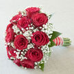 In this image, a romantic bouquet of sumptuous red roses and airy white baby's breath is captured as if resting in the calm morning light of a quiet Golders Green side street. The roses form a rounded, harmonious dome, each bloom full and velvety, their deep crimson tones suggesting passion, warmth, and a sense of timeless celebration. Between them, the fine, cloud-like clusters of gypsophila weave in and out, creating a soft mist of white that highlights the intensity of the roses without ever overshadowing them. A few slender green leaves and hints of foliage frame the blooms, adding an understated freshness that feels reminiscent of walking past the gardens near Golders Hill Park or Hampstead Heath on a mild day. The stems are gathered and wrapped with smooth ribbon, accented by delicate strings of pearls that give the handle an elegant, bridal character, as though ready to be carried from a Golders Green synagogue or registry office to a nearby reception. You can imagine the tactile richness-the cool satin of the petals, the crisp stems resting in the hand, and the fine, almost feathery touch of the gypsophila. The overall mood is intimate yet quietly grand, ideal for an anniversary dinner at home, a proposal, or the walk down the aisle. Crafted with the care of a florist who understands both tradition and modern style, this bouquet speaks fluently of enduring love, special milestones, and the heartfelt gestures shared throughout the Golders Green community.