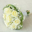 Arranged with the quiet confidence of an experienced hands-on florist, this bridal bouquet rests diagonally on a light beige, textured fabric and embodies classic wedding restraint. Seven prominent, creamy-white roses anchor the design; some unfurl fully while others hold a soft, rounded bud, together producing a gentle rhythm of ivory tones and velvet textures. Surrounding them are many small clusters of pure white gypsophila that float like mist through the arrangement, softening edges and adding an ethereal depth. Curving strands of bright green bear grass weave through the outer ring, creating gentle loops that frame the roses and introduce a clean, contemporary line among the traditional blooms. The stems are tightly bound and finished with a silvery-white satin ribbon, its surface threaded with multiple rows of tiny, iridescent pearls that glow subtly under diffuse light and suggest an heirloom quality. The bouquet's fragrance is faint and fresh-a whisper of rose-while the tactile contrast between silky petals, airy baby's breath, and smooth grass invites touch. Photographed on neutral fabric with soft, even lighting to showcase detail and craftsmanship, the arrangement communicates both purity and celebration. As a local florist serving Golders Green and nearby Finchley Road, Flowers Golders Green crafts pieces like this for brides, anniversaries, or respectful sympathy bouquets, and can adapt the same elegant palette for small ceremonies at Golders Hill Park or intimate receptions on Golders Green Road.