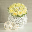 Creamy yellow roses are gathered into a compact, dome-like bouquet, their layered petals opening in gentle spirals that suggest warmth and quiet joy. Fine sprays of baby's breath weave between the blooms, their tiny white blossoms acting like delicate punctuation marks that lift and lighten the composition. The flowers sit within an airy white wicker orb, its architectural curves and tight weave providing a modern base that reads almost like a piece of gallery sculpture. Subtle curling blades of green trace the rim, framing the bouquet and adding a soft graphic edge that complements the roses' roundness.

The scent is evocative: a crisp, sun-warmed aroma reminiscent of fresh-cut fields, with an earthy undernote that grounds the sweetness of the roses-an olfactory memory you might catch while walking from Golders Green station toward Finchley Road on an early summer morning. The lighting captures each nuance of tone, making the pale yellows glow against the clean white of the basket. As a local florist I arrange pieces like this for a range of moments-congratulations, thoughtful remembrances, or understated wedding accents-and I make a point of using fresh stems sourced locally to maintain that field-fresh scent. Available for delivery across Golders Green and nearby streets, this bouquet reflects careful craftsmanship, elegant restraint, and a modern sensibility, the kind of thoughtful arrangement customers ask for at Flowers Golders Green when they want something both beautifully honest and quietly refined.