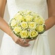 Held tenderly in the hands of a bride within the leafy avenues of Golders Green, this sunlit bridal bouquet is a symphony of softness and joy. Clusters of buttery yellow roses, their petals tinged with the gentle glow of afternoon light, nestle closely together, forming a lush dome that radiates hope and quiet exuberance. Interspersed among the blooms, fine clouds of baby's breath add a whisper of purity, evoking the charm of local churchyards in spring. The bouquet's form is gracefully defined by slender swirls of deep green grass or foliage, a subtle nod to the natural artistry found in Golders Green gardens. The bride's manicured fingers, painted in a barely-there blush, cradle the bouquet just above her white gown, adorned with intricate textures and lace. The focus is intimate-every petal, every leaf captured in detail-while the soft, creamy blur of the background allows the composition's romance to shine through. This bouquet speaks not only of love and ceremony but of the unique floral traditions cherished here in Golders Green, making it an ideal choice for any bride seeking both timeless beauty and a touch of London's local elegance on her special day.