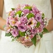 The mood is one of gentle joy as a bride from Golders Green embraces her bouquet-a rounded masterpiece brimming with pastel pink and lavender roses, refreshing lime button chrysanthemums, and delicate pink alstroemeria with maroon-flecked throats. Wisps of baby's breath, light as morning mist drifting over Golders Green streets, nestle in between, giving the ensemble an airy, romantic look. The green button chrysanthemums offer a playful energy, echoing the lively markets and green spaces just beyond the shop doors. Each bloom feels thoughtfully placed, its colour and texture creating harmony-a tactile blend of velvety petals and crisp greenery. The bouquet's base of glossy green leaves provides structure and a classic touch. As soft light spills across the wedding gown's lace, the bouquet radiates the love and anticipation that defines life's biggest moments in NW11. Evoking the artistry and warmth of a local Golders Green florist, this bouquet captures the promise of new beginnings-ideal for any bride starting her story in this vibrant North London community.