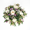 Laid out against a bright white background and viewed from directly above, this sympathy bouquet appears like a small, perfectly formed garden captured in a moment of stillness. The main impression is of creamy white roses, their petals opening slowly in gentle spirals that create soft shadows and highlights, from almost pure white at the tips to a mellow ivory and faint peach deep within the bloom. Some roses are fully open and expansive, while others remain partially closed, their layered petals wrapped closely together, giving the arrangement a sense of quiet depth and continuity. Twining through and around these roses are slim stems of purple alstroemeria in bud, each one showing a delicate blend of colour: the pointed tips washed in lavender and soft violet, descending into tinges of pink and then cool, fresh green toward the stem. Only a few buds are beginning to part, just enough to hint at the streaked, trumpet-shaped flowers they will become. Dancing between the more substantial blooms, sprays of white baby's breath scatter like fine mist, each tiny blossom forming part of a cloud-like halo that softens and lightens the whole design. Encircling everything is a lush collar of deep green leaves, broad and slightly glossy, gently cupping the flowers and giving the bouquet its rounded, hand-tied look. The colour harmony of whites, purples, and greens feels especially calming, much like a slow walk through the quieter corners of Golders Hill Park or a still moment in a Golders Green home filled with shared memories. This arrangement seems designed to sit respectfully by a bedside, at a small memorial, or on a windowsill overlooking the streets of NW11, offering a tender, living token of sympathy, love, and support.