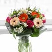 A symphony of colour and emotion, this stunning bouquet captures the vibrancy of Golders Green's local character. At its center, bold orange and gentle peach gerbera daisies bloom in harmonious contrast, their plush petals and deep chocolate centers forming a radiant focal point. Rich fuchsia roses provide an elegant counterbalance, their tightly layered petals infusing the design with intimacy and passion. Crisp white alstroemeria and clusters of tiny spray roses peek between the main blooms, adding sparkle and a whisper of soft fragrance that calls to mind spring mornings wandering around Childs Hill Park. The lush, deep green foliage - including wide, folded aspidistra leaves - creates a graceful frame that grounds the bouquet in organic tranquility and echoes the area's abundant natural beauty. Arranged in a tall glass vase, with vibrant stems visible, the bouquet glistens under gentle, diffused light, suggesting clarity and renewal. Designed for a memorable celebration or heartfelt gesture-perhaps as a cheerful gift delivered to a loved one on Golders Green Road-this arrangement highlights the skilled touch of local florists and the uplifting essence of the community.