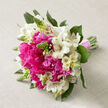 Resting on a softly textured beige linen backdrop, this hand-tied bouquet looks as though it has just been placed down after a quiet moment of admiration, the kind of arrangement you might see waiting on a table in a Golders Green townhouse before a wedding. At its core, generous hot pink peonies bloom in full splendour, their ruffled petals layered so densely that the centres are almost hidden, creating a plush, cushiony effect. Surrounding them, white alstroemeria flowers open gracefully, each petal pale and smooth with subtle russet and pink flecks near the throat, adding a refined, almost painterly touch. Threaded between these main blooms are upright green buds and slender stems, giving the bouquet height and a hint of movement, as if the flowers are stretching toward the light that falls gently from one side. Rich green foliage supports the design from beneath, some leaves emerging in small arcs that cradle the flowers, others forming a deeper base that shapes the bouquet into a softly rounded dome. The stems are gathered in a close bundle, wrapped with a light pink ribbon tied snugly yet simply, leaving the green stems clean and visible at the base - a classic hand-tied style often chosen for brides walking down the aisle or for elegant gifts delivered around Temple Fortune and Golders Green Road. The overall impression is one of fresh abundance and understated romance, a bouquet that carries the scent of new beginnings, quiet excitement, and carefully curated beauty.