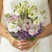 There's a poetic charm in this hand-tied bridal bouquet as seen through the lens of a Golders Green wedding morning. Layers of white lisianthus, petals ruffled and luminous, open into pools of creamy light, nestled with clusters of pastel-pink and lavender stock that seem to float in a fragrant, textured cloud. Unopened buds and curling tips of fresh bear grass lend a graceful modern twist, their rich green expertly echoing the leafy avenues that crisscross Golders Green. At the base, a ring of star-like purple allium stands out - its geometric, playful forms anchoring the softness above, much like the bold accents found in local NW11 gardens. The bouquet is lovingly supported in the bride's softly manicured hands, her nails a gentle blush, with a veil of lace from her gown casting a delicate, blurred shimmer in the background. Every element - from the architectural contrasts to the subtle, sunlit hues - offers a sense of quiet anticipation and joy, ideal for an elegant spring wedding on Golders Green's historic streets. The bouquet's artistry and freshness evoke the unique warmth of local celebration, promising memories as lasting as their soft perfume.