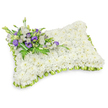 A serene, hand-shaped memorial pillow crafted entirely from hundreds of small, pristine white chrysanthemum heads sits like a soft cloud against a crisp white backdrop. The chrysanthemums are densely packed to form a uniform, cushion-like surface, each tiny bloom lending a plush, almost velvety texture that suggests quiet rest and gentle comfort. The tribute is distinctively rectangular with softly rounded corners and a subtly raised profile that echoes the shape of a sleeping pillow; a faint shadow beneath gives the piece reassuring three-dimensionality. Around the edge, a pale lime-green satin ribbon is pleated into neat scallops, its cool, fresh hue drawing a tender line between the pure white floral mass and the surrounding space. In the upper-left corner a composed spray of accent blooms provides contrast and focus: layered white lisianthus with their delicate, ruffled petals sit beside deeper purple lisianthus, some still in tight buds, their color imparting dignity and a quiet note of remembrance. Feathery fern fronds and elegant dark green leaves weave through this cluster, adding soft movement and a natural freshness; a broad, darker green leaf wrap secures the stems and folds neatly beneath. The scent is faintly floral, the chrysanthemum's clean note balanced by the sweet, tea-like perfume of lisianthus. Presented as a graveside or chapel tribute, the arrangement reads as an expression of peace and reverence-calm, crafted, and comfortingly simple-suitable for services in Golders Green, nearby Hampstead Garden Suburb, or quiet remembrance gatherings at Golders Hill Park.