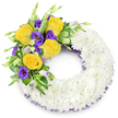 Against a clean white studio background sits a mourning wreath shaped as a perfect ring - a soft, cloud-like circle of densely packed white spray chrysanthemums that reads immediately as a quiet statement of purity and peace. The chrysanthemums are layered so closely their many tiny petals blend into a uniform, cushiony surface, the texture almost asking to be felt; the open centre of the wreath keeps the traditional circular form clear and dignified. From the upper left curve a single, carefully placed spray arcs gently toward the top: several fully opened bright yellow roses, their butter-gold petals unfurling in slow spirals, pair with richly saturated purple lisianthus (Eustoma) whose ruffled, cup-shaped blossoms add velvet depth. A few pale lavender-tinged lisianthus buds and pale green, rounded buds peek through, giving the cluster a living, forward-moving quality. Interwoven behind the blooms is an assortment of fresh green foliage - glossy, rounded leaves with faint variegation, slender fern fronds and a scattering of delicate filler - which provides both structural support and a natural tonal bridge between the white ring and the colourful spray. Along the inner and outer edges of the chrysanthemum base a subtle dark purple mesh ribbon peeks out, its fine texture echoing the lisianthus tones and tying the composition together. The arrangement catches soft, even light that emphasizes the chrysanthemum's matte softness and the roses' satiny sheen, and a faint, comforting rose scent seems almost perceptible in the stillness. As a local florist familiar with Golders Green memorial traditions - including services at Golders Green Crematorium and quiet gatherings near Golders Hill Park - I see this wreath as a calm, respectful tribute meant to hold memories with tenderness and grace.