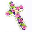 A generous floral cross arrangement fills the frame against a spotless white background, angled slightly so the top left arm reaches toward the viewer, giving the piece a gentle sense of depth and presence. The outer shape of the cross is crisply outlined with a dense fringe of small white spray chrysanthemums, the tiny blooms forming a soft, cloud-like halo that suggests purity and remembrance. Beneath this pristine border runs a neat band of light green folded ribbon or foliage, its fresh hue subtly echoing the calm greenery of nearby Golders Hill Park in Golders Green and adding a refined finishing touch. Within this border, the centre of the cross is richly packed with flowers in a harmonious, uplifting palette. Large roses in radiant pink and soft, creamy yellow or peach tones form the main focal points, their open, layered petals bringing a sense of tenderness and love. Bright lime-green button chrysanthemums are scattered thoughtfully among the roses, their rounded, slightly textured heads adding a playful, contemporary rhythm that still feels appropriate for a Christian funeral tribute. Threaded between these larger blooms are clusters of smaller purple and deep violet flowers-likely lisianthus or statice-which add depth and a gentle sense of solemnity. The overall design is lush and full, with each flower placed carefully so that colour and texture flow smoothly from top to base. Bathed in clear, even lighting, every stem and petal appears fresh and vivid, suggesting a tribute prepared the same day for a memorial service or graveside farewell in Golders Green, offering both comfort and a quiet celebration of a life well lived.