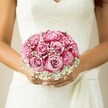 Bathed in the quiet radiance of a Golders Green morning, I imagine the sensation of holding this bouquet-a charming fusion of romance and exuberance. Each rose, two-toned and vibrant, opens in meticulously curled spirals: their hearts softly blush, their outer petals singing with the richer notes of fuchsia and magenta, much like the subtle transitions of the seasons in north London. Between these blooms, baby's breath laces the bouquet with airy, veil-like softness, diffusing the arrangement into something ethereal and comforting. The bride's hands, slightly sun-warmed and manicured with care, hold the flowers close against a wedding gown adorned in tactile, floral lace and finished with a sweeping sash-an ensemble reminiscent of traditional celebrations near Golders Green Road. The composition invites a gentle promise: the dewy fragrance of roses mixed with the innocence of gypsophila, the cool weight of petals eased against lace, and the electricity of expectation in the air. This is the kind of bouquet that tells a story-of hope, joy, and love blooming right in the heart of Golders Green, perfect for capturing memories on a truly unforgettable day.