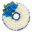 A bespoke funeral tribute shaped into the numeral '0', captured against a clean white background to show every careful detail. The core of this memorial number is densely covered in hundreds of small white spray chrysanthemums, their cushion-like florets overlapping to form a continuous, cloud-soft surface that suggests quiet comfort and repose. Tracing both the outer and inner edges of the '0' is a deep royal-blue border-pleated satin ribbon that is ruffled into a scalloped frame and echoes the intense hue of the roses; the ribbon's satin sheen catches light and gives the tribute a formal, finished silhouette. Dominating the upper left curve of the figure, three vivid royal blue roses are clustered together, their petals unfurling from tight centers into velvety spirals; a few glossy, dark green leaves tuck gently beneath them, lending depth and a natural counterpoint to the blue-and-white palette. The overall impression is balanced and dignified: cool, clean whites soften the sting of loss while the saturated blues offer a reserved, heartfelt focal point-appropriate for marking an age, a date, or a personal number at a memorial service. The textures read clearly-the papery, slightly aromatic chrysanthemums against the plush rose petals and the smooth pleats of ribbon-so someone unable to see the image can imagine the touch and mood. As a local florist familiar with Golders Green and the routes to the crematorium on Hoop Lane, we arrange such personalised number tributes with quiet respect; this design reads as both a visual symbol of remembrance and a tactile gesture of care for mourners gathering to honour a life.