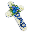A traditional Christian funeral cross made from flowers is shown laid out on a clean white background, the simple setting drawing full attention to its calm, dignified beauty. The entire cross is fully covered with tightly set white spray chrysanthemums, each head neatly overlapping the next to form a soft yet structured surface, like a white quilt of petals. Following the outline of the cross, a royal blue satin ribbon runs continuously around the edge, gathered and gently ruffled so that it creates a shimmering border that contrasts strongly with the pure white flowers. In the centre, where the horizontal and vertical arms meet, there is a prominent cluster of rich royal blue blooms, including rounded, ruffled carnations and more slender spires of delphinium- or orchid-like flowers that rise slightly from the base. These blue flowers are framed by dark green fern fronds and small leafy stems, which add depth, texture, and a sense of natural garden foliage. On the vertical arm, the tribute becomes deeply personal: the word DAD is carefully shaped from the same royal blue ribbon, each letter formed by folded and looped fabric and anchored onto the white chrysanthemum background. This ribbon inscription transforms the cross into a heartfelt memorial for a father, expressing both grief and affection. The lighting feels even and gentle, with only a faint shadow beneath, emphasizing the three-dimensional quality without distraction. This floral cross would be fitting for a funeral or graveside tribute in Golders Green, perhaps carried from a nearby florist studio near Finchley Road to a service or burial where family gather to say a final goodbye.