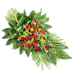 This image shows a beautifully composed elongated sympathy spray, laid out on a crisp white background so that its colours and contours appear especially vivid and clear. The arrangement forms a graceful, tapering shape, broader at the left and narrowing to a soft point on the right, much like a flowing leaf or a gentle wave. At its centre, deep red roses unfold in velvety layers, some in tight buds and others more open, symbolising different stages of life and memory. They are joined by red gerbera daisies with dark eyes and ruffled red carnations, together creating a strong, heartfelt core of crimson colour. Scattered among these are bright lime green chrysanthemum pompons, almost spherical in form, their fresh, zesty hue bringing contrast and a contemporary touch that recalls the vibrant plantings around Golders Green's local parks and residential gardens. Small white filler blooms, airy and delicate, drift between the larger flowers, softening the overall effect.
Surrounding this central ribbon of red and green is a generous layer of mixed foliage. Broad, glossy leaves provide a dark, polished backdrop, while lighter, feathery ferns and assorted textured greens add depth and a natural, garden-like feel. At the lower right, long, slim leaves spray outward to emphasise the elongated silhouette, giving the design a sense of movement and poise. At the upper left, neatly gathered upright stems and leaves create a vertical accent; one broad leaf wraps gracefully around their base, adding a sculptural, modern detail. Crafted in a style often chosen for funerals and memorial services across Golders Green, this spray offers a serene, dignified tribute, blending colour, form, and emotion into a single, harmonious farewell.