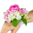 Delicate and poised, this wrist corsage reads like a small poem of spring - a wearable bouquet captured against a clean white backdrop. At its centre sits a large, fully opened deep fuchsia-pink rose whose tightly layered petals spiral outward with a velvety sheen; the rose gives off a soft, warm perfume that one can almost sense from the image. Surrounding it are clusters of blush-pink hydrangea florets that create a plush, cloud-like base, their papery textures catching soft highlights and adding gentle volume. Scattered between the hydrangea are pristine white alstroemeria (Peruvian lilies), four- to six-petalled and marked with pale green streaks near their throats, introducing bright points of contrast and a slender, graceful silhouette. On the right-hand side a small spray of pale green alstroemeria buds and a few barely open pink blooms promise more unfolding life, while broad, rich emerald leaves cradle the composition and deepen the colour palette. The corsage is fastened to the wearer's left wrist by a refined multi-strand bracelet of tiny, lustrous white pearls that nestles along the skin and trails slightly toward the back of the hand; the visible forearm and hand show a light-to-medium skin tone, lending scale and intimacy. Lit with soft, even light that emphasises texture rather than harsh shadow, the arrangement feels intimate and timeless - ideal for a prom or a wedding moment. As a local touch, imagine this piece prepared for a North London celebration near Golders Hill Park, an elegant choice that balances youthful romance and careful floristry craftsmanship familiar to Golders Green florists.