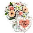A tender Mother's Day gift arrangement is presented against a bright white background, giving the scene a calm, gallery-like feel, as if carefully styled in a Golders Green florist's workshop. The focus is a lush mixed bouquet gathered in a clear, slightly rounded glass vase, its neck encircled with a simple wrap of rustic twine that hints at artisan craftsmanship. Soft pastel tones dominate the flowers: peach-pink roses are fully open, displaying layered spirals of petals that curl gently at the edges, while several peach gerbera daisies with dark chocolate centres add a cheerful, daisy-like boldness. Between these larger blooms drift generous wisps of white baby's breath, their tiny blossoms creating a delicate, misty veil around the arrangement. Smaller white chrysanthemum-style flowers, each with a fresh hint of pale green at the centre, are tucked in to build volume and texture, suggesting the abundant look of a hand-picked garden bunch from nearby residential streets off Hoop Lane. Rich green foliage, likely a mix of common bouquet greens, forms a verdant background, breaking up the pastels and giving the bouquet shape and structure. Just behind the flowers, partially hidden, sits a modest white card with hints of coloured writing, suggesting a personal Mother's Day message without drawing focus. To the right of the vase, resting against it, a large heart-shaped Mylar balloon brings a playful, celebratory touch. The balloon is white and sprinkled with shiny gold and silver dots, with a soft peach heart at the centre bearing the phrase HAPPY Mother's DAY in bold black lettering and elegant script. Altogether, the image evokes warmth, appreciation, and the quiet joy of sending a Mother's Day bouquet for same-day delivery around Golders Green.